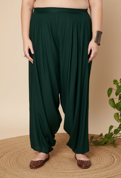 Woman wearing dark green cowl salwar pants on a beige background